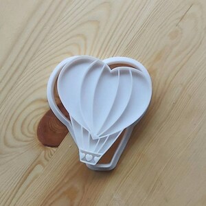 May include: White plastic cookie cutter shaped like a hot air balloon with three hearts at the bottom.