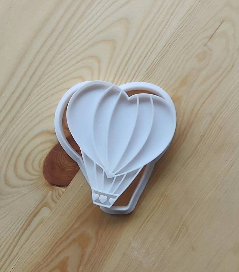 May include: White plastic cookie cutter shaped like a hot air balloon with three hearts at the bottom.