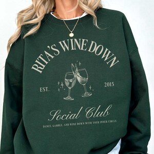 a woman wearing a green sweatshirt with a picture of two glasses of wine on it