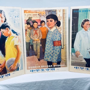 May include: Three vintage Chinese propaganda posters with the text "Middle School Student Code of Conduct" in blue and white lettering. The posters feature illustrations of students in various settings, including a classroom, a street scene, and a group of students playing sports. The posters are in good condition and have a faded, vintage look.