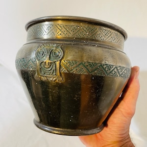 Puede incluir: Un macetero vintage de latón con un diseño de búho y detalles verdes. El macetero tiene un patrón geométrico alrededor de la parte superior e inferior.