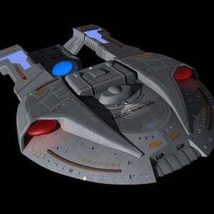 May include: A gray spaceship model with red and blue accents, featuring the text "U.S.S. APPALACHIA NCC-52136". The model has a saucer-shaped primary hull, two warp nacelles, and a secondary hull. The background is black.
