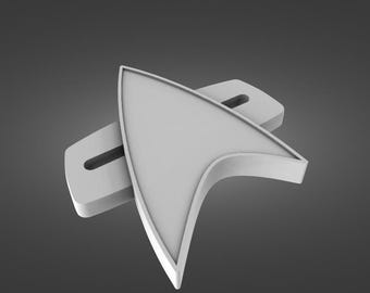 Op de afbeelding: Een wit plastic Star Trek-insigne, een gestileerde deltavorm, is gemonteerd op een witte plastic basis. Het insigne is een populair symbool uit de Star Trek-franchise.