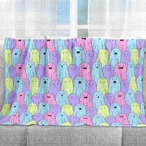 May include: A soft, plush throw blanket featuring a repeating pattern of pastel-colored ghosts with different facial expressions. The ghosts are in shades of pink, blue, green, and purple.
