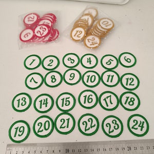 Peut inclure: Un ensemble de 24 cercles en feutre vert et blanc avec les chiffres de 1 à 24. Les cercles sont disposés en rangées et en colonnes. Une règle se trouve en bas de l'image.
