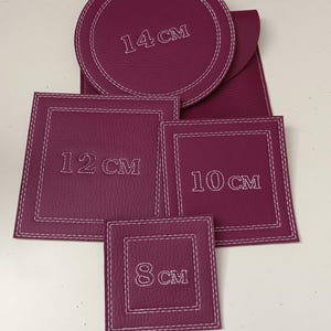 Peut inclure: Ensemble de dessous de verre en cuir bordeaux de différentes formes et tailles. Le plus grand est rond, 14 cm de diamètre, et les autres sont carrés, mesurant 8 cm, 10 cm et 12 cm. Chaque dessous de verre a des coutures blanches.
