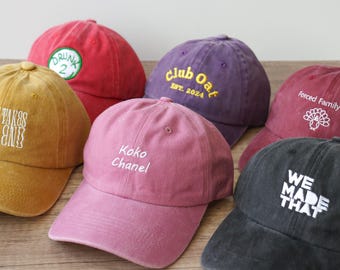 May include: A collection of six baseball caps in various colors, including yellow, red, purple, pink, and black. Each cap features embroidered text or a design, such as "Taty Takes Top End," "Koko Chanel," and "We Made That."