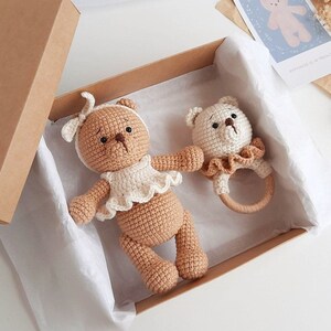 Puede incluir: Dos osos de peluche de crochet en una caja de regalo marr&oacute;n. Un oso es marr&oacute;n con un volante blanco y el otro es blanco con un volante y un sonajero de madera.