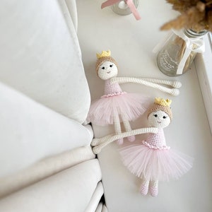 Op de afbeelding: Twee gehaakte ballerinapoppen met roze tutu's en gele kronen. De poppen liggen op een wit oppervlak.