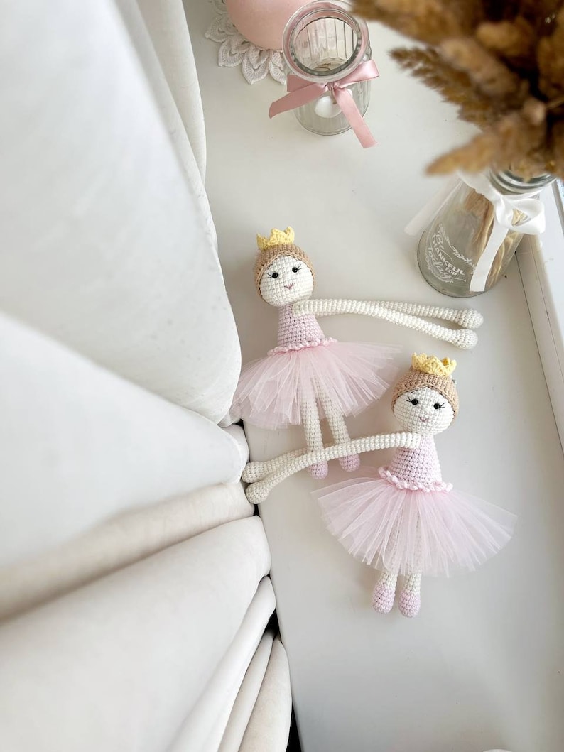 Op de afbeelding: Twee gehaakte ballerinapoppen met roze tutu's en gele kronen. De poppen liggen op een wit oppervlak.