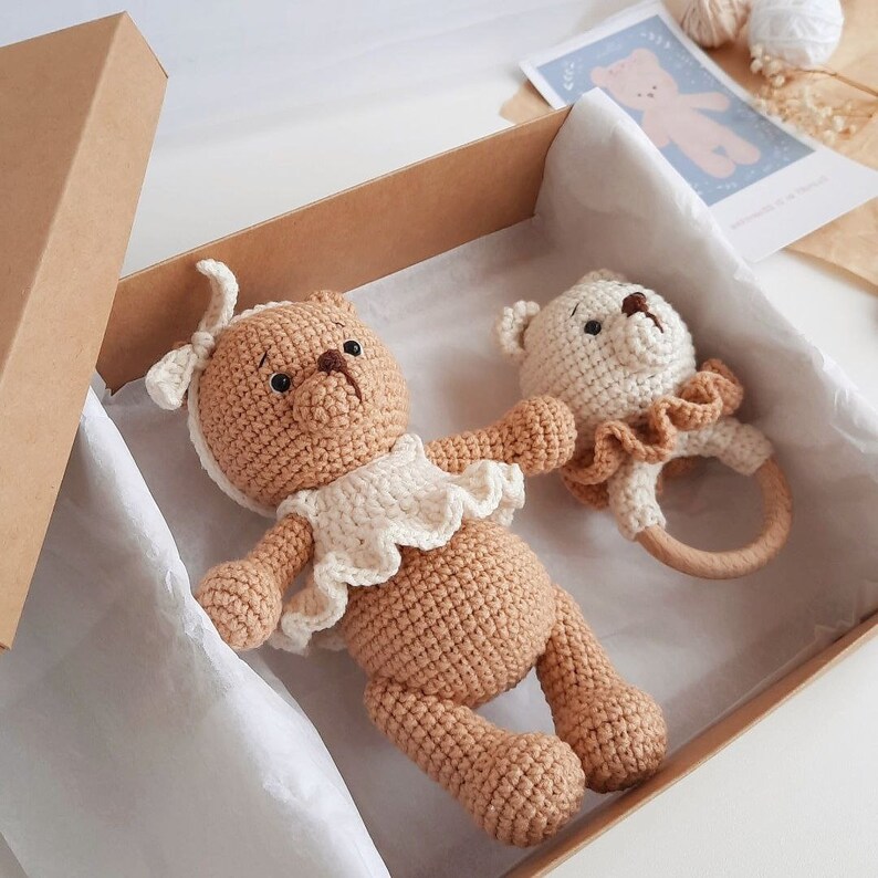 Puede incluir: Un oso de peluche de crochet marr&oacute;n que lleva un vestido blanco de crochet y una diadema blanca de crochet. El oso de peluche est&aacute; en una caja marr&oacute;n con papel de seda blanco. Hay un oso de peluche blanco m&aacute;s peque&ntilde;o de crochet con un anillo de madera unido.