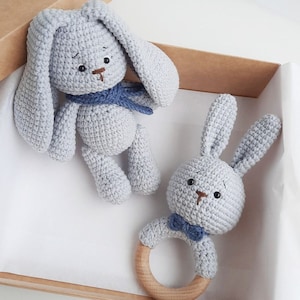 May include: Two crocheted stuffed animals, a bunny and a rabbit, in a light blue color. The bunny is holding a wooden teething ring.
