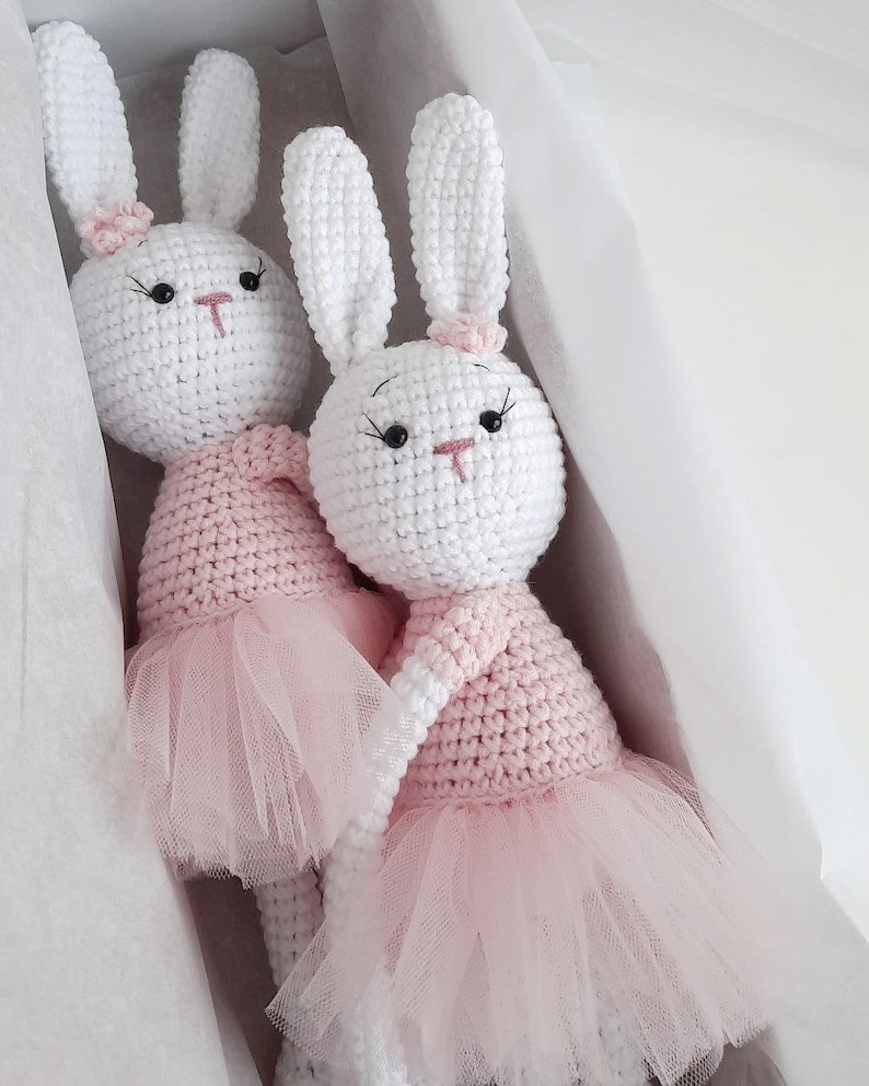 Puede incluir: Dos mu&ntilde;ecas de conejo de crochet blanco con tut&uacute;s rosas. Los conejos tienen ojos negros y narices rosas. Est&aacute;n sentados en una caja blanca.
