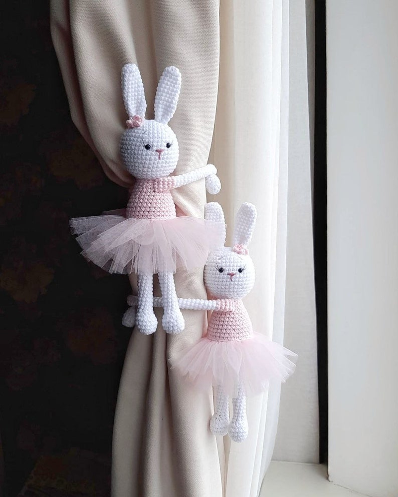 Puede incluir: Dos lazos de cortina de conejito de crochet blanco con tut&uacute;s rosas. Los conejos se agarran a la cortina con los brazos.