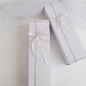 May include: Two white gift boxes tied with twine and white ribbon. Each box has a white wax seal with a design.