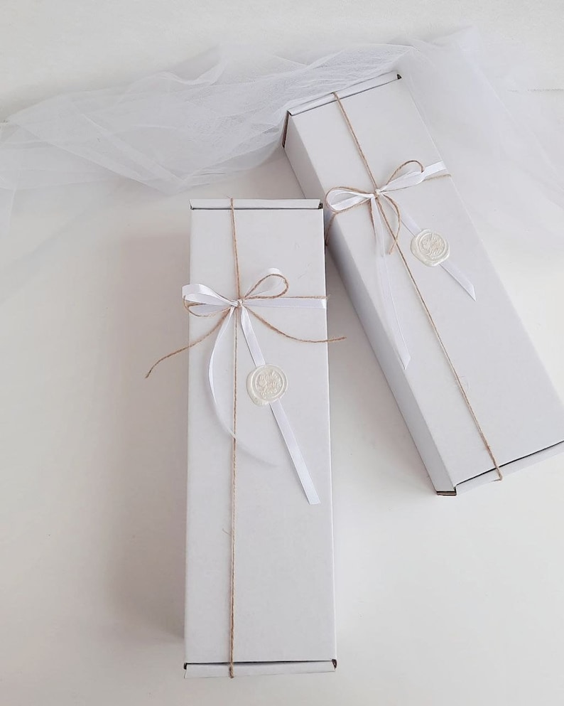May include: Two white gift boxes tied with twine and white ribbon. Each box has a white wax seal with a design.