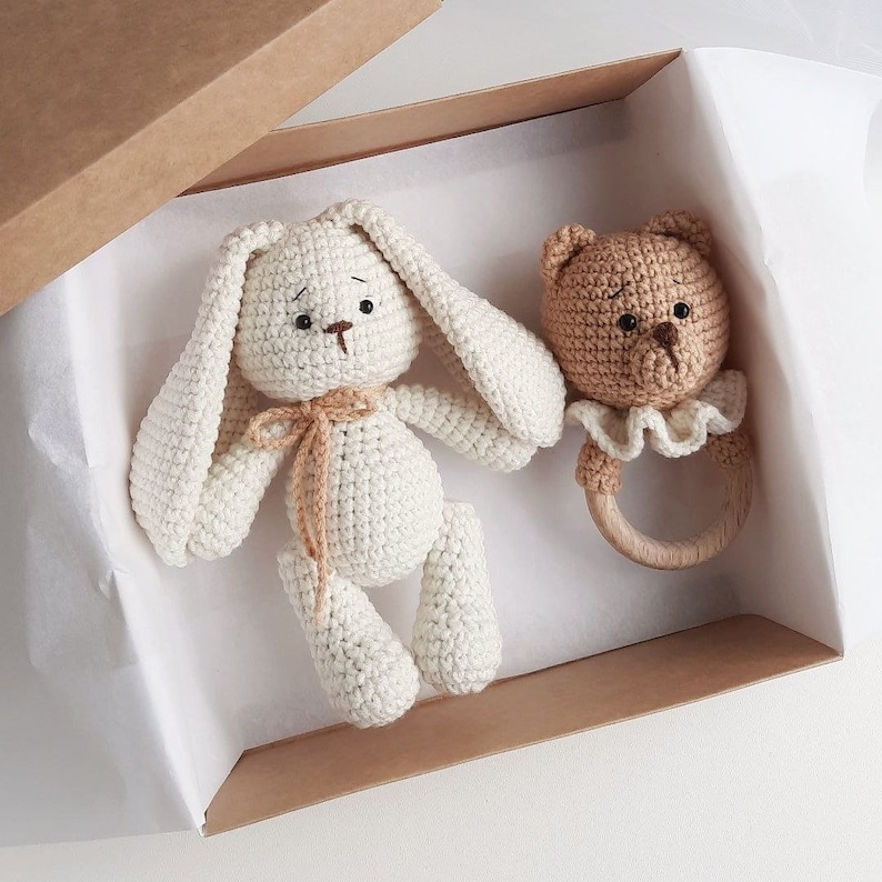 May include: A white crocheted bunny and a brown crocheted bear rattle in a brown gift box with white tissue paper.