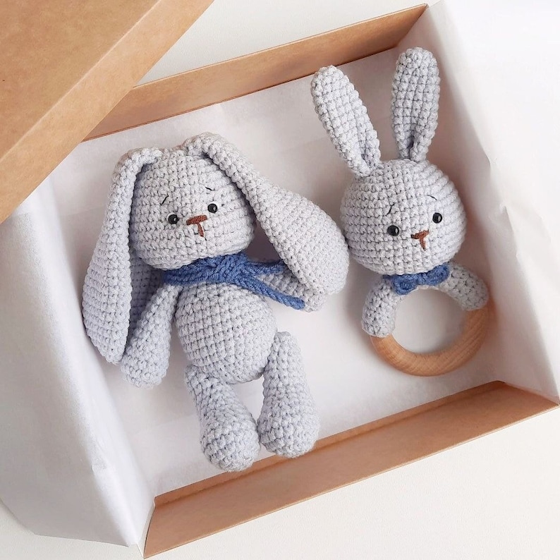 May include: Two crocheted gray bunny toys. One bunny is a rattle with a wooden ring. The other bunny is larger and has a blue scarf.