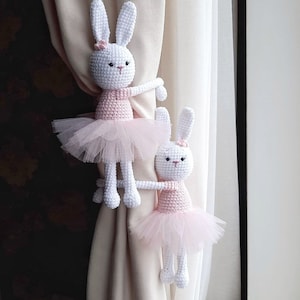 Puede incluir: Dos mu&ntilde;ecas de conejo de crochet blanco vestidas con tut&uacute;s rosas se utilizan como ataduras de cortinas. Los conejos sostienen las cortinas beige con sus brazos.