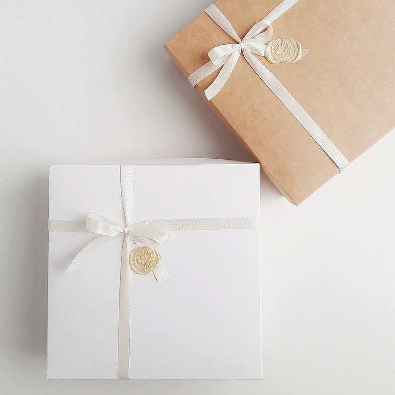 May include: Two gift boxes with white ribbon and wax seals. One box is brown and the other is white.