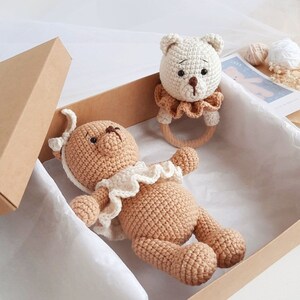 Puede incluir: Dos osos de peluche tejidos a crochet en una caja marr&oacute;n. Un oso es marr&oacute;n y tiene un volante blanco alrededor del cuello. El otro oso es blanco y tiene un anillo de madera sujeto a su cuello.