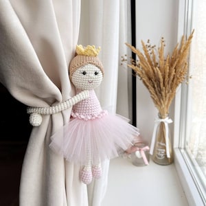 Op de afbeelding: Een gehaakte ballerinapop met een roze tutu en een gele kroon, gebruikt als gordijnband.
