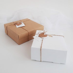 Puede incluir: Dos cajas de regalo, una marr&oacute;n y otra blanca, est&aacute;n atadas con cuerda y decoradas con etiquetas en forma de coraz&oacute;n.
