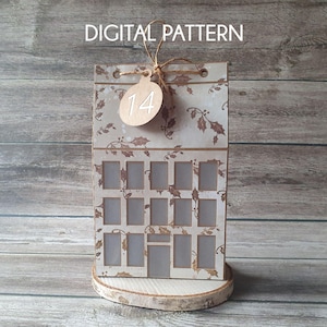 May include: A handmade Advent calendar with a rustic design. The calendar features a light-colored background with holly leaf patterns and small rectangular openings. A wooden tag with the number 14 hangs from the top. The words "DIGITAL PATTERN" are at the top.