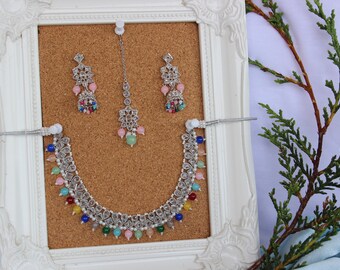 May include: A silver necklace with a floral design and colorful beads, matching earrings and a matching tikka.