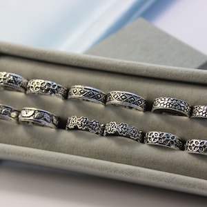 Op de afbeelding: Een set van tien zilveren ringen met verschillende ingewikkelde ontwerpen, gepresenteerd in een grijze fluwelen doos.