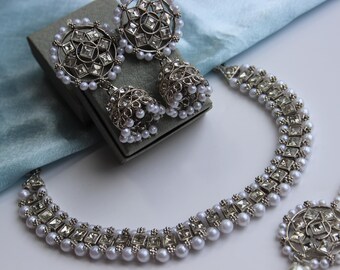 May include: A silver necklace and earrings set with white pearls and clear rhinestones. The necklace is a choker style with a delicate chain and a row of square-shaped rhinestones. The earrings are dangle style with a round rhinestone cluster and a pearl drop.