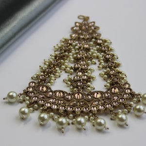 May include: A gold-tone hairpiece with pink and clear stones and white pearl accents. The hairpiece is designed in a cascading style with multiple tiers of stones and pearls.