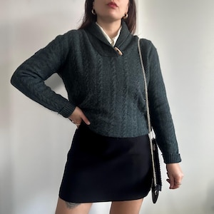 May include: A dark green cable knit sweater with a wide collar and a single button closure. The sweater is paired with a black mini skirt and a gold chain strap bag.