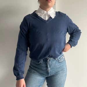 Può includere: Un maglione blu navy a maniche lunghe con scollo a V e un colletto in pizzo bianco.