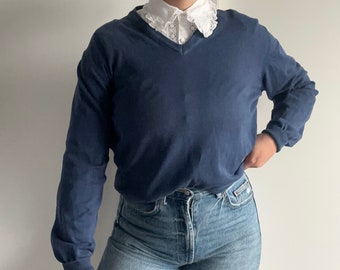 Könnte beinhalten: Ein marineblauer Langarm-Pullover mit V-Ausschnitt und einem weißen Spitzenkragen.