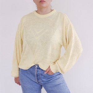 Può includere: Un maglione di maglia giallo pallido con un motivo geometrico. Il maglione ha maniche lunghe e un collo rotondo.