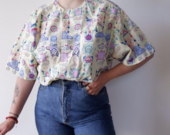 May include: A yellow short-sleeved shirt with a colorful geometric pattern. The shirt has a round neckline and a relaxed fit.