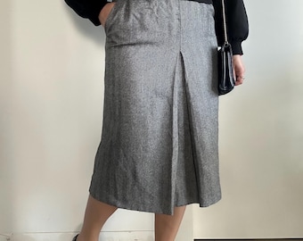 May include: A gray tweed skirt with a pleated front and a black sweater. The skirt is knee-length and has a fitted waist. The sweater has long sleeves and a round neckline.