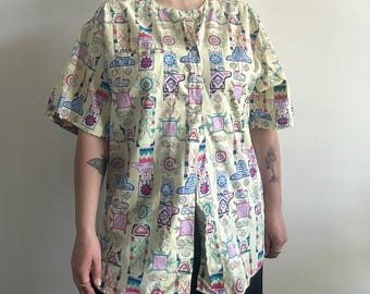 May include: A yellow button-up shirt with a short sleeve and a colorful geometric pattern. The shirt has a mandarin collar and a front button closure.