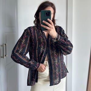 Può includere: Una camicia nera trasparente con bottoni, righe colorate e un motivo geometrico. La camicia ha maniche lunghe e una vestibilità rilassata.
