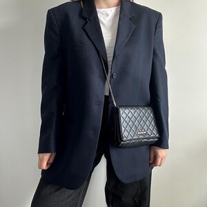 Könnte beinhalten: Ein marineblauer Blazer mit einem einzigen Knopfverschluss und eine schwarze gesteppte Umhängetasche mit einer silbernen Kettenkette.