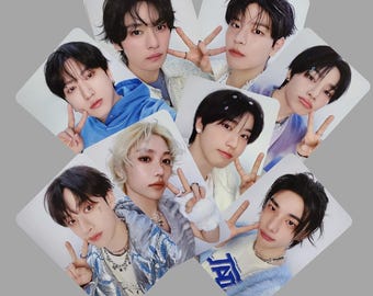 May include: A set of eight photo cards featuring different members of a boy band. Each card has a white background and features a close-up portrait of a young man with a light blue and white outfit. The men are smiling and making peace signs with their hands.