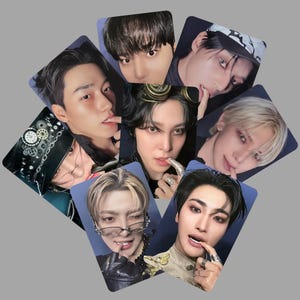 May include: A collection of eight photo cards featuring close-up portraits of individuals with various hairstyles and expressions. The cards have a blue background and are arranged in a slightly overlapping pattern. The subjects are wearing accessories like goggles and rings.