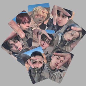 May include: A collection of nine photo cards featuring portraits of individuals in various poses. Each card displays a different person, with diverse hairstyles and expressions. The cards are held up by hands, creating a dynamic arrangement against a desert backdrop.