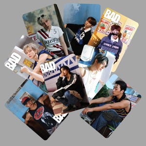 May include: A collection of seven rectangular photo cards featuring various individuals in diverse outfits, each card prominently displaying the word BAD in white capital letters. The images showcase different poses, clothing styles, and settings, including casual wear, graphic tanks, and layered tops, with some cards featuring posters or tiled backgrounds.