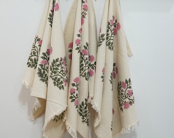 May include: Three cream-colored kitchen towels with a pink and green floral print hang on a black metal rack. The towels have a fringed edge.