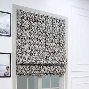 Puede incluir: Una cortina romana con un estampado floral en blanco y negro. Está instalada dentro de un marco de ventana blanco. La tela es lino puro. El nombre de la impresión es Manikarnika.