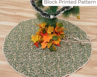 May include: A round, green Christmas tree skirt with a floral block print pattern. The skirt has a beige border and is tied with beige fabric ties. The text "Block Printed Pattern" is in a white box. A small Christmas tree and fall leaves are on top.