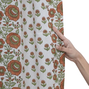 May include: A white fabric curtain featuring a repeating block-printed pattern of large orange flowers with green centers and stems, interspersed with smaller orange floral motifs. The textile displays a clear, detailed botanical print design.