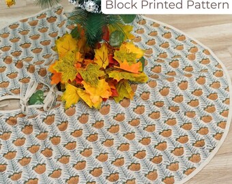 May include: A round Christmas tree skirt with a block-printed pattern of orange flowers and blue-gray leaves on a cream background. The skirt has a white border and a tie closure. The text "Block Printed Pattern" is visible.